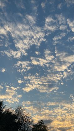 the sky is filled with clouds as the sun goes down in the distance behind some trees