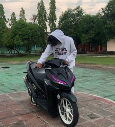 a person standing next to a black motorcycle on a brick walkway with trees in the background