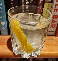 a glass filled with ice and lemon wedges on top of a wooden table next to books