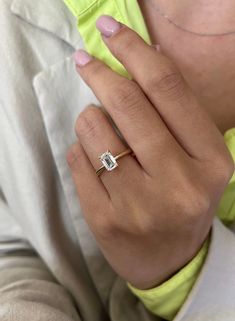 a woman's hand wearing a gold ring with a square shaped diamond on it