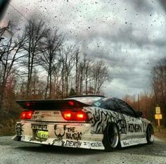 a white car with graffiti on it's tail lights parked in front of a forest