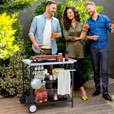 two men and a woman standing next to a bbq grill with drinks on it