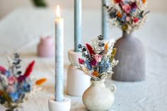 three vases with flowers are sitting on a table next to candles and other decorations