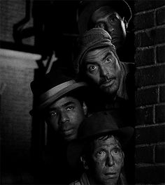 four men standing next to each other in front of a brick wall with their eyes wide open