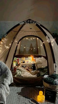 the inside of a tent is lit up with fairy lights and blankets on the floor