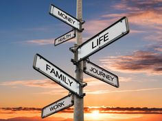 street signs pointing in different directions with the sun setting behind them