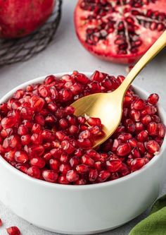 a white bowl filled with pomegranate and a golden spoon in the bowl