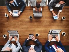 four people sitting at a table working on their laptops with coffee cups in front of them