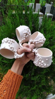 two hands holding white vases in front of green plants