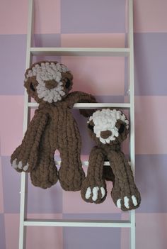 two crocheted stuffed animals sitting on top of a ladder against a pink and purple wall