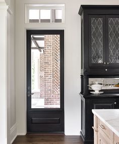 a kitchen with black cabinets and white counter tops next to a door that has glass panels on it