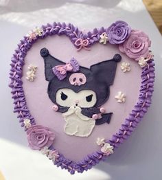 a heart shaped cake decorated with purple icing and pink flowers on the side, in the shape of a cat