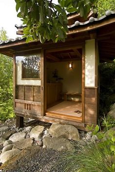 a small wooden structure with a door and window on top of rocks in front of trees