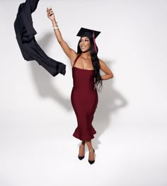 a woman in a graduation gown and cap is holding up a black jacket over her head