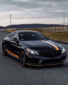 a black car with orange stripes on the front driving down a road next to a field