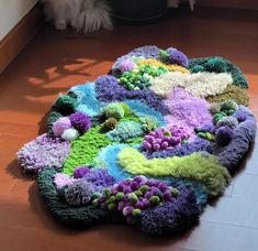 a cat is sitting on the floor next to a rug made out of various colored yarns