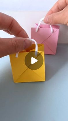 someone is opening an origami bag with a string on the handle and another paper bag in the background