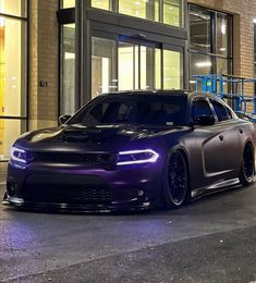 a purple dodge charger parked in front of a building at night with its lights on