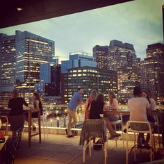 people are sitting at tables on the roof of a building with city lights in the background