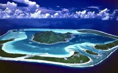 an island in the middle of the ocean surrounded by land and water with clouds above it