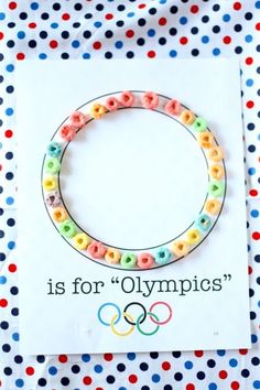 a bracelet made out of cereal beads with the olympic logo on it, sitting in front of a card that says is for olympics