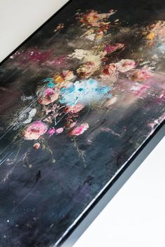 a painting with flowers on it sitting on top of a white tablecloth covered in black and pink paint