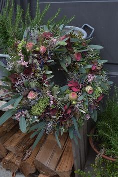 a wreath with flowers and greenery on top of wooden logs in front of a building