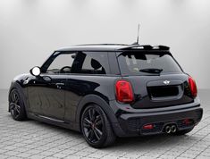 the back end of a small black car on a tile floor with lights in the background