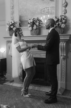 a man and woman standing in front of a fire place holding each other's hands