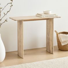 a white vase sitting next to a wooden table on top of a hard wood floor