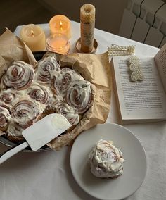 a table topped with a cake covered in icing next to an open book and candle