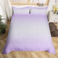 a bed with purple sheets and pillows on top of wooden flooring next to a potted plant