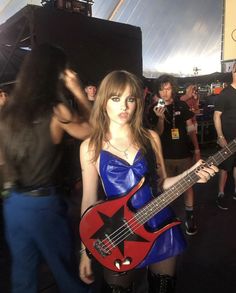 a woman in a blue dress holding a red and black bass guitar at a music festival