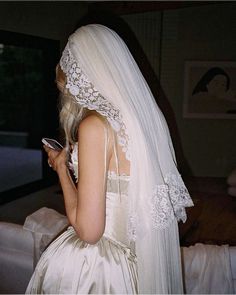 a woman in a wedding dress looking at her cell phone while she is wearing a veil