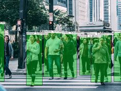 people walking across a crosswalk in the city, with green images on them and buildings behind them