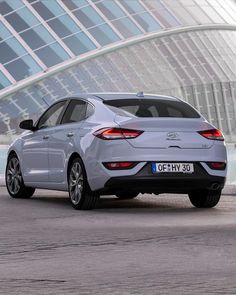 the rear end of a silver car parked in front of a large building with glass windows