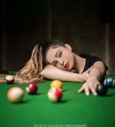 a woman laying on top of a pool table next to billiards and balls