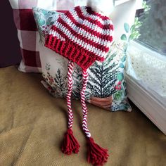 a red and white knitted hat sitting on top of a pillow next to a window