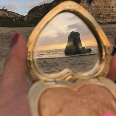 someone is holding up a compact mirror to show the reflection of a rock in the water