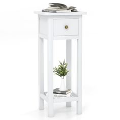 a white end table with a book on top and a potted plant in the corner