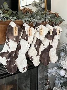 three stockings hanging from a mantel decorated with greenery