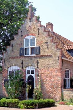 an old brick house with white windows and black shutters on the front, surrounded by greenery