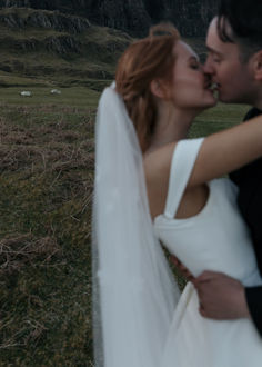 a bride and groom kissing in the middle of an open field with sheep behind them