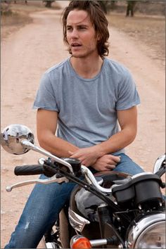 a man sitting on top of a motorcycle in the middle of a dirt road next to trees