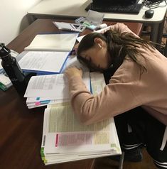 a woman sitting at a desk with books and papers in front of her, covering her eyes