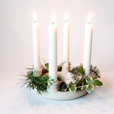 four white candles with greenery and evergreen leaves in a bowl on a white background