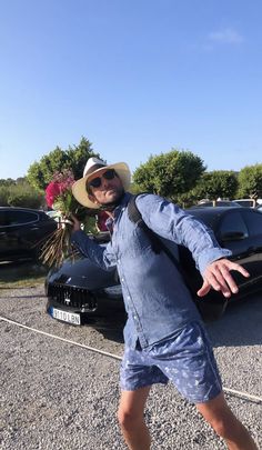 a man in blue shirt and hat standing next to a black car with flowers on it