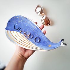 a person holding a blue whale shaped object with gold rings on it's nose