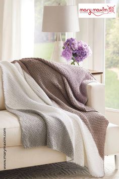 a couch with a blanket on top of it next to a vase filled with flowers