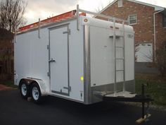 a white enclosed trailer parked in front of a brick building with a ladder on the side